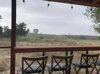 three chairs sitting on a porch with a view of a field at Modern wine country barn house in Temecula