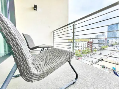 a rattan chair on a balcony with a view of a city at The Leo - One Bedroom Apartment w Private Balcony in San Diego
