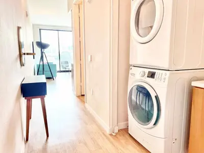 a white washing machine in a room with a stool at San Diego Skyline - Downtown Apartment in San Diego