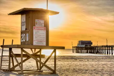 a bench on the beach with a pier in the background at Newport Beach Simplicity III in Newport Beach