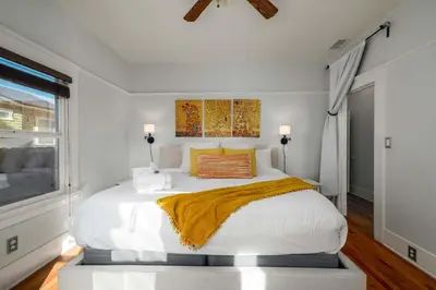 a white bedroom with a large bed with a yellow blanket at South Park Charmer - Close to Zoo - Backyard Oasis in San Diego