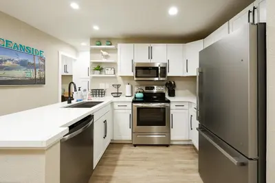 a kitchen with white cabinets and a stainless steel refrigerator at Oceanside Beach Condos in Oceanside