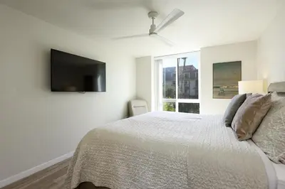 a white bedroom with a bed and a flat screen tv at Oceanside Beach Condos in Oceanside