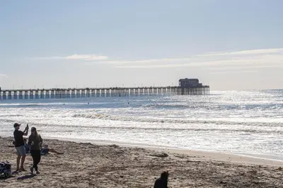 a group of people walking on the beach with a pier at Oceanside Beach Condos in Oceanside