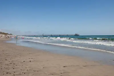 a beach with people standing in the water and a pier at Oceanside Beach Condos in Oceanside