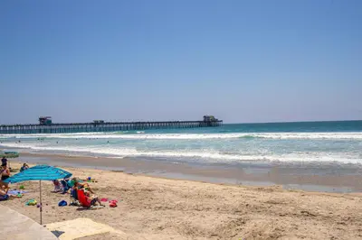 a beach with people sitting on the sand and a pier at Oceanside Beach Condos in Oceanside