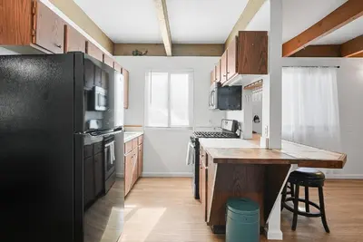 a kitchen with a black refrigerator and wooden cabinets at Mission Bay Condo - Steps to Sand, Dining, AC, Parking & Shops! in San Diego