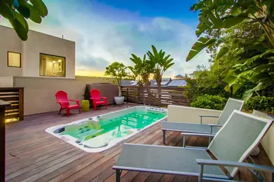a patio with a hot tub and chairs on a deck at Sunset Cliffs Modern Luxury Estate w Ocean Views, Oversized Spa, AC, Yard! in San Diego