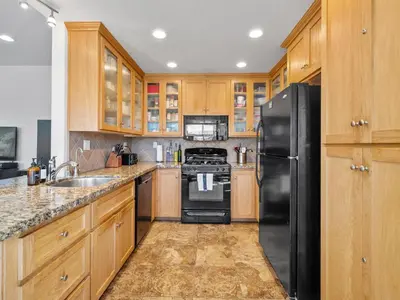 a kitchen with wooden cabinets and a black refrigerator at Pacific Beach Paradise - Near the Beach w AC, Garage, Fast Wifi & Private Patio! in San Diego