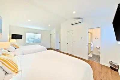 a white bedroom with two beds and a television at Shores Perfection - Spa, AC, Pet Friendly, Parking, Fire Pit & Massive Private Yard! in San Diego