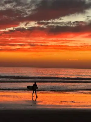 a man walking on the beach with a surfboard at Brooks Beach Vacations Cottage G5 Oceanside in Oceanside