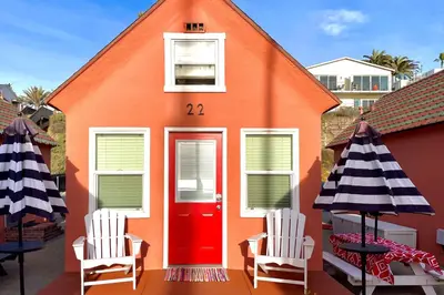 an orange house with two chairs and a red door at Sandcastle Cottage 22 in Oceanside