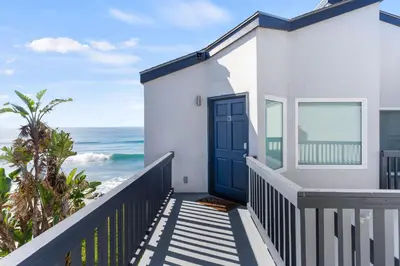 a white house with a blue door and the ocean at Romantic Getaway - Luxury Oceanfront Studio - Private Balcony - Fireplace in Oceanside