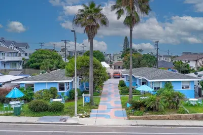 a city street with blue houses and palm trees at Walk To Beach - EV Charger - Outdoor Dining - 2BR in Carlsbad