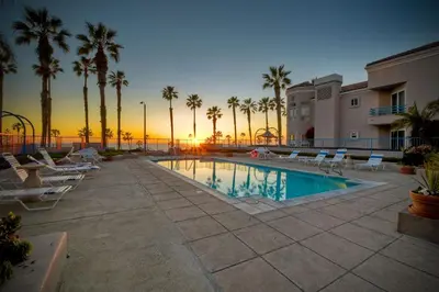a pool with chairs and palm trees at sunset at Ocean View, Pool, Hot Tub, Steps To Pier, Gated in Oceanside