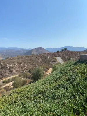 a grassy hill with a road and mountains in the background at Acres of Bliss - A hillside getaway in Ramona