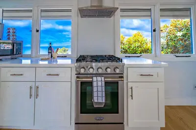 a kitchen with white cabinets and a stove and windows at Blue Water View Condo in Prime Coastal Locale in San Diego