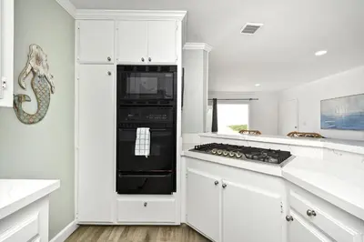 a kitchen with white cabinets and a black stove top oven at Oceanfront Triplex on Boardwalk with Ocean Views and Patio in Newport Beach