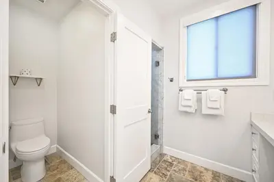 a white bathroom with a toilet and a window at Upscale Home with Rooftop Deck, Jacuzzi, & Firepit in Newport Beach