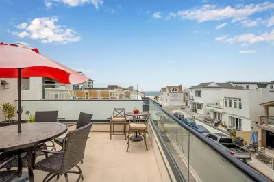 a balcony with tables and chairs and a red umbrella at 50 Steps to the Sand on 39th St - Newport Beach in Newport Beach