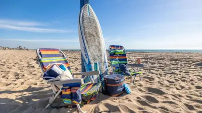two chairs and a surfboard on the beach at Ocean Breeze I by AvantStay Steps to the Beach in Newport Beach