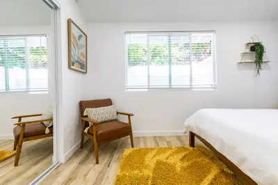 a bedroom with a bed and a chair and windows at Stylish Casita min from the beach ! in San Juan Capistrano