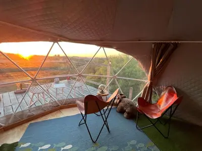 a person sitting in a tent with a dog and chairs at Sunset Dome - Outdoor Shower/Composting Toilet in Valley Center