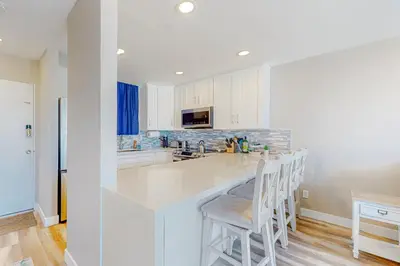 a kitchen with white cabinets and a bar with stools at Bayside Retreat in San Diego
