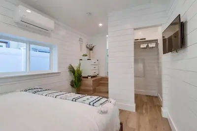 a white bedroom with a bed and a television at Breezy Bayside Cottage in San Diego
