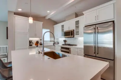 a kitchen with white cabinets and a stainless steel refrigerator at Newly Built Bayside Dream, Fire Pit & Bay Views in San Diego