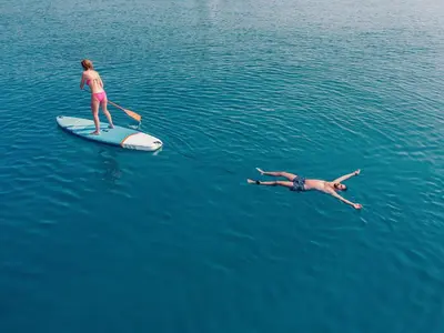 a woman on a paddle board and a man swimming in the water at The Boardwalk Hotel in San Diego