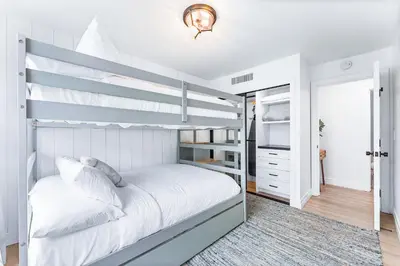 a white bedroom with a bunk bed with a ladder at Luxury Ground S Oceanfront Unit with Boardwalk Lounge Firepit - AC in San Diego