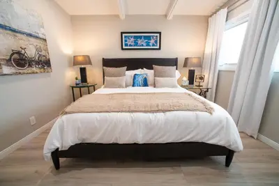 a bedroom with a large bed and two windows at La Jolla Windansea Luxury Apt in San Diego