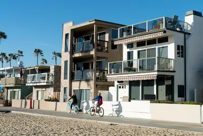 two people riding bikes down a street in front of a building at Abigail - Beachfront in Newport Beach