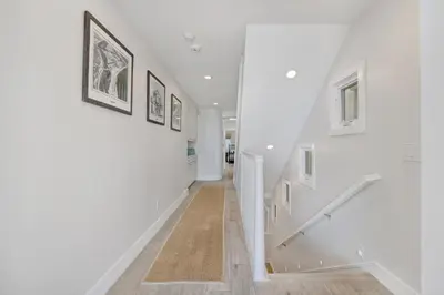 a hallway with white walls and stairs with paintings on the wall at 3312 W Oceanfront in Newport Beach