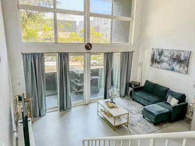 a living room with a green couch and large windows at Beautiful Loft in Little Italy SD with Parking in San Diego