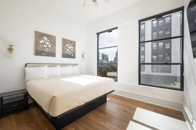 a white bedroom with a bed and two windows at The Beau Hotel Downtown San Diego Gaslamp Quarter in San Diego