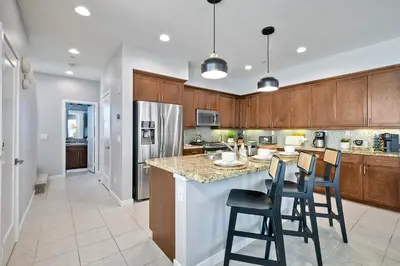 a kitchen with wooden cabinets and a island with bar stools at Blocks To Beach - Coastal Beach Decor - Garage Parking - Gated Community - 30 Day Fully Furnished in Oceanside