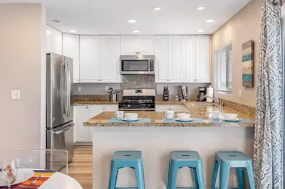 a kitchen with white cabinets and blue stools at Beachside Oasis in Newport Beach Steps to Balboa Park, Pier, and The Fun Zone! in Newport Beach
