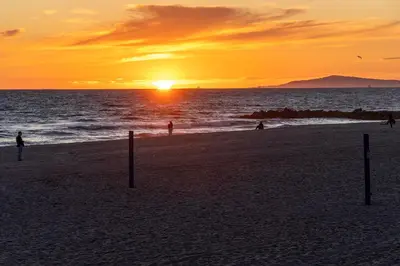 a sunset on a beach with people in the water at Spacious 5BR Beach Home with Ocean Views in Newport Beach