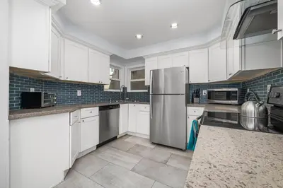 a kitchen with white cabinets and a stainless steel refrigerator at Giant Newport Duplex - Surf, Sand, Playground, Parking in Newport Beach