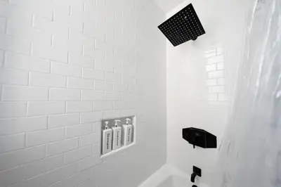 a white tiled bathroom with a shower and a sink at City Lights and Rooftop Nights by Rather Be Properties in San Diego