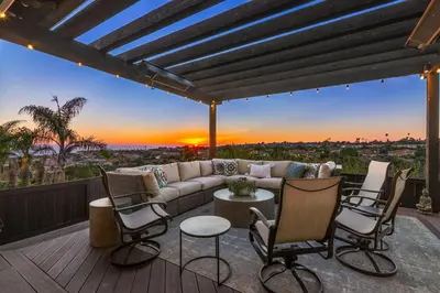 a patio with a couch and chairs on a deck with a sunset at Timeless Spanish Villa with Panoramic Ocean Views in San Diego