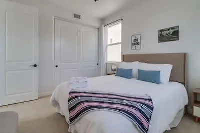 a white bedroom with a large white bed with blue pillows at Rooftop Patio Hot Tub AC Beach & Bay Views in San Diego