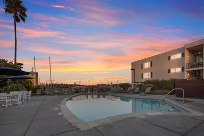 a swimming pool in front of a building with a sunset at Serene Harborfront Condo | Unbeatable Views & Coastal Charm in Oceanside