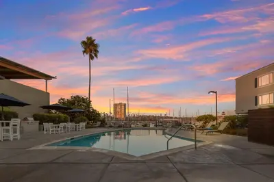 a pool with chairs and a palm tree and a sunset at Oceanside Harbor Getaway | Steps to Sand, Shops & Restaurants in Oceanside