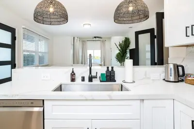 a white kitchen with a sink and two pendant lights at Newly Built Coastal Home with Yard in San Diego