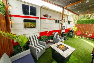 an rv with chairs and a table and a fire pit at Darling Daisy Retro RV Adventure in El Cajon