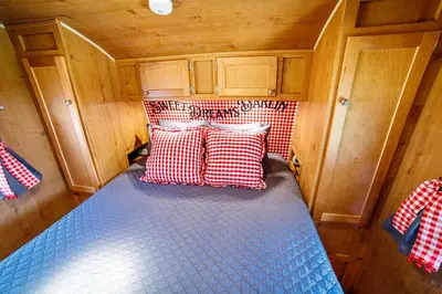 a bed in a small room with red and white pillows at Darling Daisy Retro RV Adventure in El Cajon