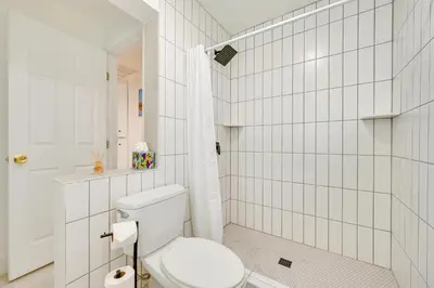 a bathroom with a toilet and a white tiled wall at House Kitsune - Steps to Beach in Oceanside